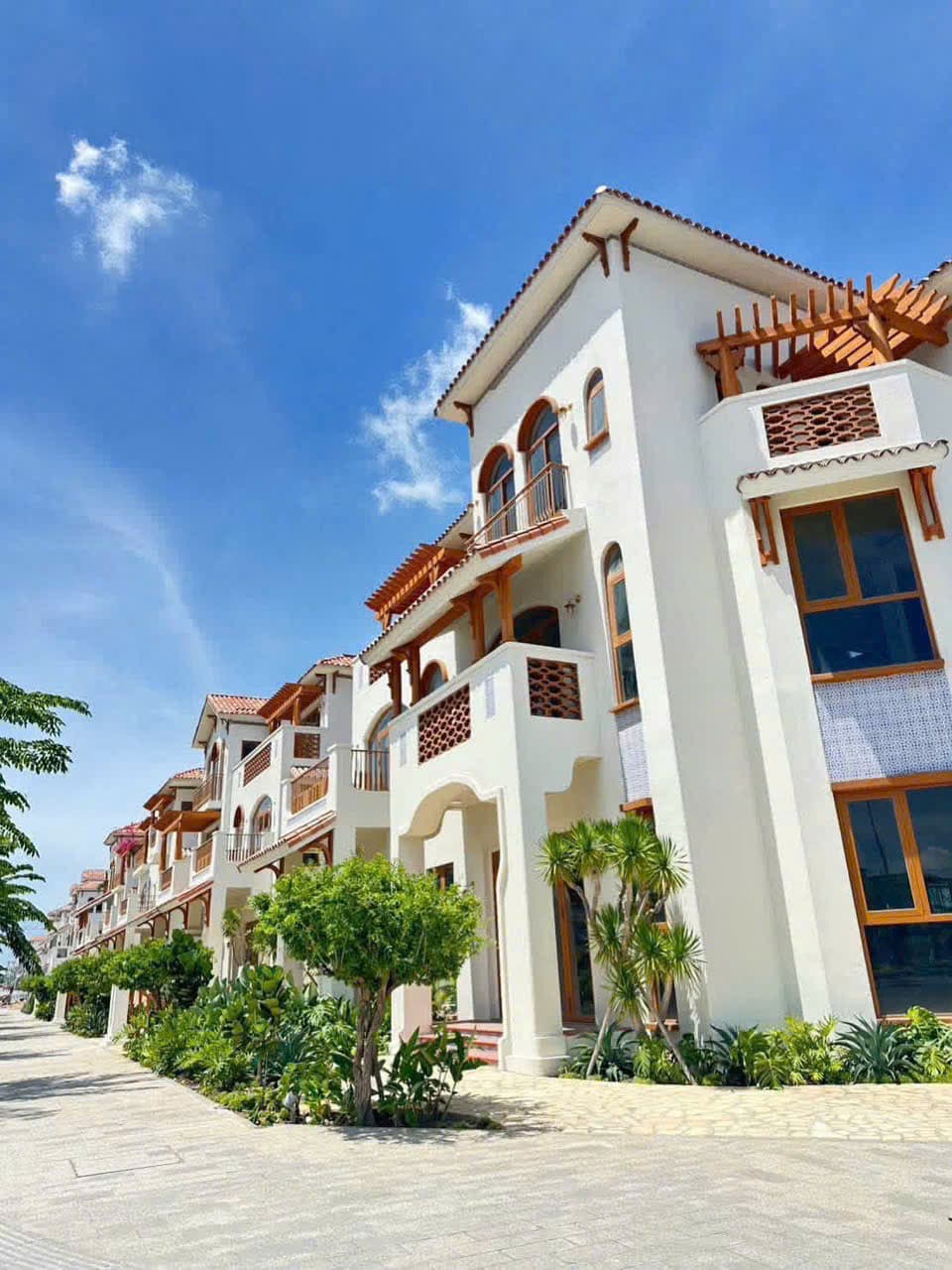Dãy nhà phố trắng nối dài dọc lối đi lát đá, cây cảnh xanh mướt dưới trời trong