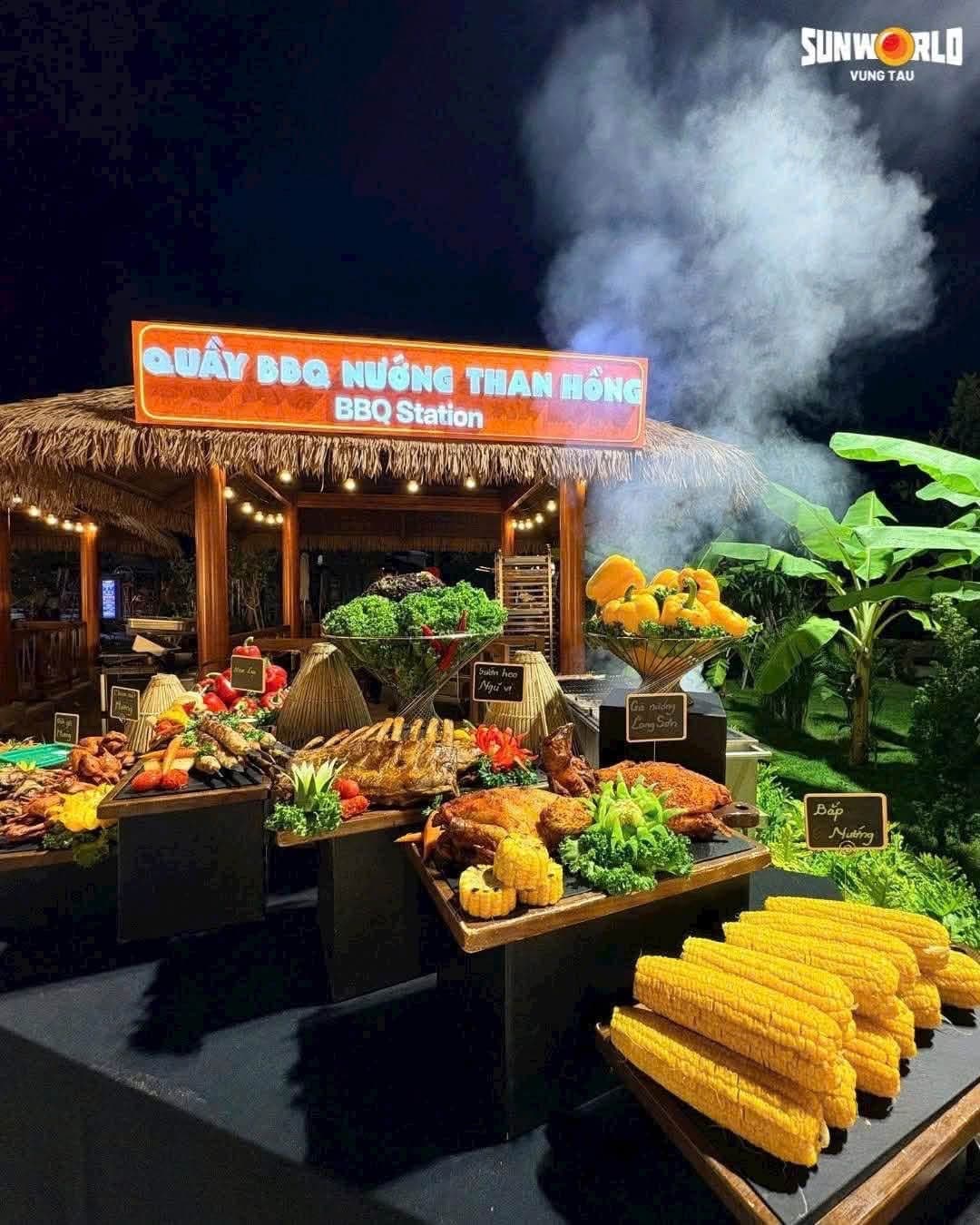 Quầy tiệc nướng BBQ mái lá ban đêm với hải sản, bắp nướng và khói bốc lên